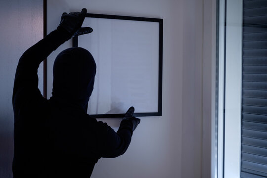 Burglar stealing a painting from an house wall