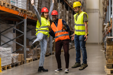 Group of warehouse workers celebrating teamwork and success with cheerful expressions