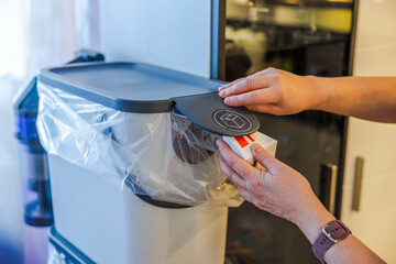 Woman's hands placing carton packaging into modern recycling bin with plastic bag and smart lid in...