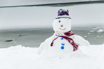 Bonhomme de neige avec un seul oeil, un chapeau et une &eacute;charpe, devant un lac gel&eacute;