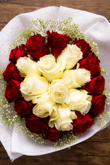 Red and White Rose Bouquet with baby breath flowers symbolizing love and passion bouquet is wrapped in delicate white paper and rests on a rustic wooden background closeup top view