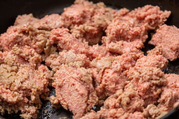 Frozen ground beef in a frying pan with vegetable oil is turned over with a spatula