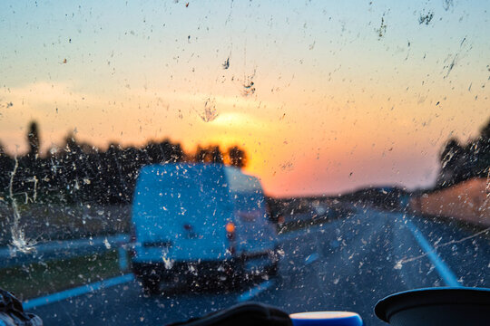 Sunset view through a dirty car windshield on the highway with a van in motion, focusing on travel, visibility, and road safety concerns. Transportation, logistics, road traffic. Copy space