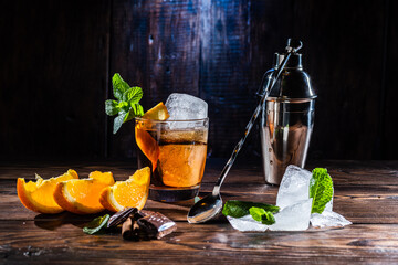 A glass of whiskey and a large ice cube. Steel shaker and bartender's spoon. Sliced citrus and mint.