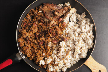 A frying pan showcases a mix of seasoned rice and beans alongside white grains, topped with a piece of grilled chicken, creating an inviting meal ready to eat.