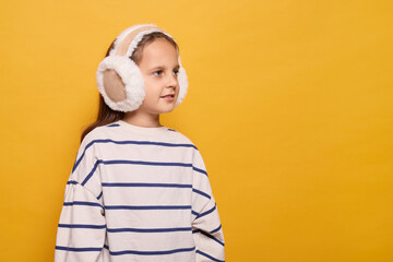 A girl is dressed in a striped sweater and warm ear muffs, smiling softly while posed against a...