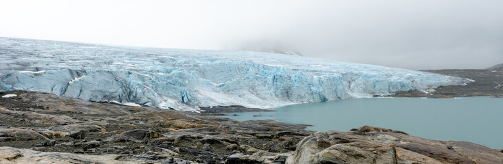 Stunning panoramic view of the Austdalsbreen glacier front and the turquoise Styggevatnet lake in Jostedal, Norway, on a cloudy day, showcasing unspoiled rugged natural beauty with no people