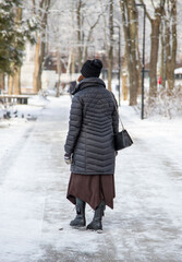 A woman wearing a black coat and a black hat is walking on a snowy path