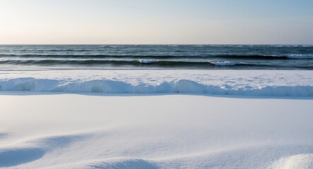 A pristine beach in winter where soft white snow contrasts with the dark blue ocean waves creating a stark and beautiful landscape