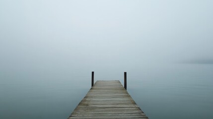 Fototapeta premium Misty lake with wooden pier extending into fog.