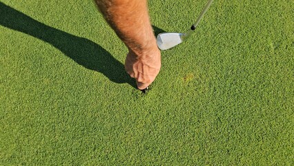 Hand holds golf tee while preparing for a successful shot on a lush green putting green in the...