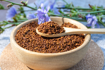 Ground chicory root on a wooden spoon and chicory flowers on a rustic wooden background. Alternative medicine. Healthy drinks. chicory drink