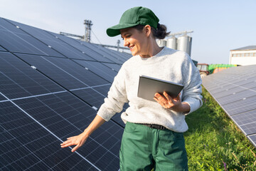 Female farmer with digital tablet on a modern farm using solar panels. Agricultural silos in the...