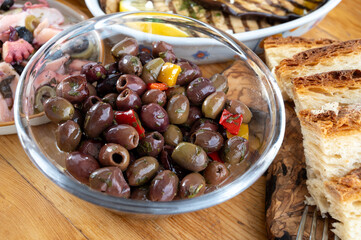 Obraz premium Pickled olives, grilled eggplant, octopus seafood salad, artichokes, vegetables on wooden table, variety of tasty Italian starters, antipasti, tapas