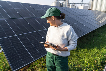Female farmer with digital tablet on a modern farm using solar panels. Agricultural silos in the...