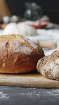 Vertical close-up shot of freshly baked loaves of artisan bread resting on wooden board on kitchen table