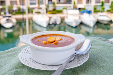 Homemade tasty fish or bisque soup with croutons and view on yacht boats and houses of Port Grimaud, French Riviera, France. Food of Provence