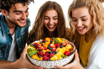 Group of friends joyfully sharing a large fruit salad on a white background in a cheerful gathering