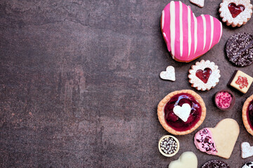 Valentines Day baking and sweets side border with a variety of cookies, chocolates and sweet treats. Top view on a dark stone background with copy space. Love and hearts theme.
