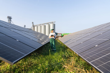 Female farmer with digital tablet on a modern farm using solar panels. Agricultural silos in the...