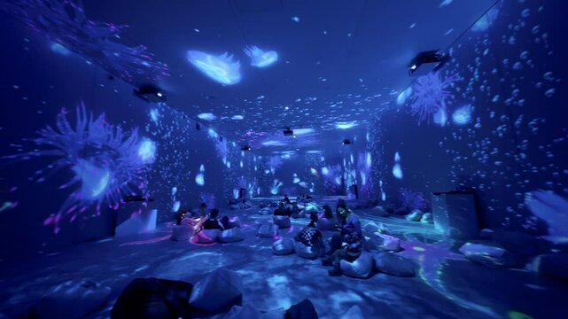 Augmented reality immersive exhibition. People in the room. Virtual reality themed museum. Children and adults watching and listening to the augmented show on headphones. Imersive room with people.