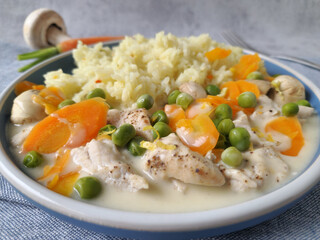 Chicken fricassee with carrots, peas, and mushrooms served with jasmine rice on a blue plate