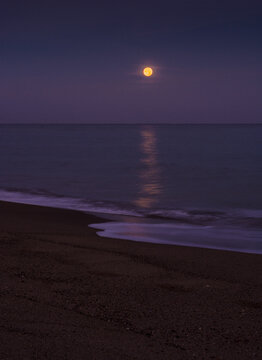 Moonlight reflection on the sea surface at night on sandy beach and calm waves, Full moon over the sea at night, Night sea illuminated by moonlight, Moon over sea or ocean in Mediterranean Sea Algeria