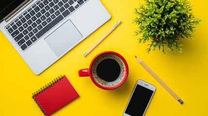 Laptop, coffee cup, smartphone, and red notebook on a vibrant yellow workspace with green plant decor