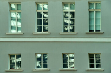 The wall of the old building, painted light green, has many windows, and in the windows you can see the play of shadows and light in the reflection, magical abstract paintings in the windows