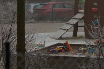 Winter empty playground, showcasing a slide, spring rider, and various toys, stands still in a picturesque snowy setting, evoking tranquility. Cars on the background.