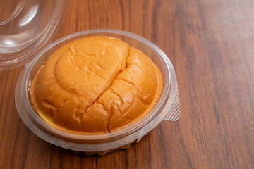 Round butter bun in plastic packaging on a wooden table surface, top view
