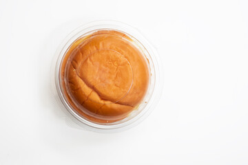 Round butter bun enclosed in plastic packaging on white background