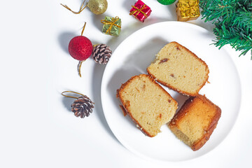 Three slices of Christmas fruit cake on a white plate surrounded by pinecones and decorative ornaments
