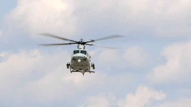 A United States Marine Corp Bell UH-1 Huey attack helicopter armed with rocket launchers hovers in front of the camera in this slow motion shot.