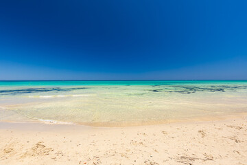 Krajobraz morski, piaszczysta plaża i wybrzeże, żółty piasek, widok na lazurowe morze, niebieski kolor nieba, wyspa Djerba, Tunezja. Tapeta, egzotyczne tło © anettastar
