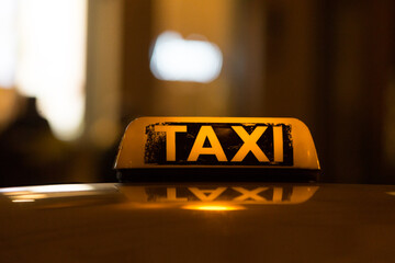 Bright yellow taxi sign on the roof of a car in a close-up view. Urban transportation highlights the convenience and accessibility of taxi services in the city. Close-Up of Yellow Taxi Sign on a Car. © Alena