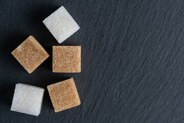 White and brown sugar cubes on black slate background. Top view.
