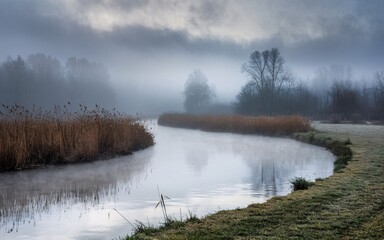 Fototapeta premium Foggy Riverbend, Misty river meandering through serene winter landscape.