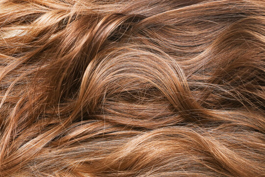 Hair background. Closeup of a woman's hair. Beautifully styled brown hair with natural shine and soft curls. Wavy hairstyle pattern.
