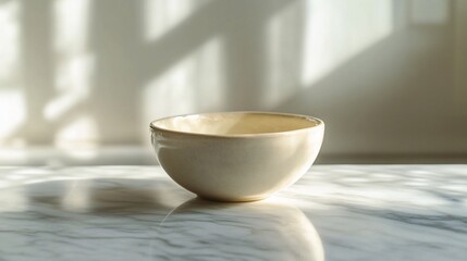 Fototapeta premium Small beige ceramic bowl on marble surface in sunlight.