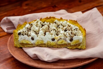 Authentic banoffee cake with banana and caramel sauce filling sprinkled with grated dark chocolate and coffee . English traditional pie