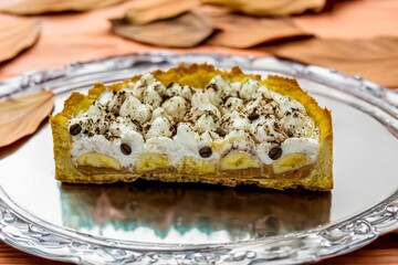 Authentic banoffee cake with banana and caramel sauce filling sprinkled with grated dark chocolate and coffee . English traditional pie