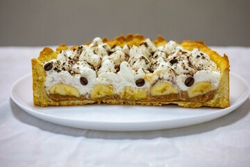 Authentic banoffee cake with banana and caramel sauce filling sprinkled with grated dark chocolate and coffee . English traditional pie