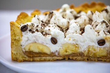 Authentic banoffee cake with banana and caramel sauce filling sprinkled with grated dark chocolate and coffee . English traditional pie