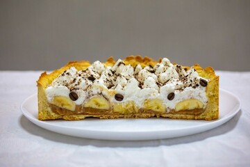 Authentic banoffee cake with banana and caramel sauce filling sprinkled with grated dark chocolate and coffee . English traditional pie