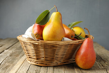 Ripe juicy pears in wicker basket on wooden table against grey background
