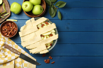 Flat lay composition with raw homemade apple pie and ingredients on blue wooden table. Space for...