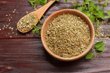 Dried oregano in bowl, spoon and green leaves on wooden table, top view