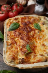 Delicious cooked lasagna in baking dish, basil and tomatoes on table, closeup