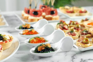 Many different tasty canapes on white marble table, closeup